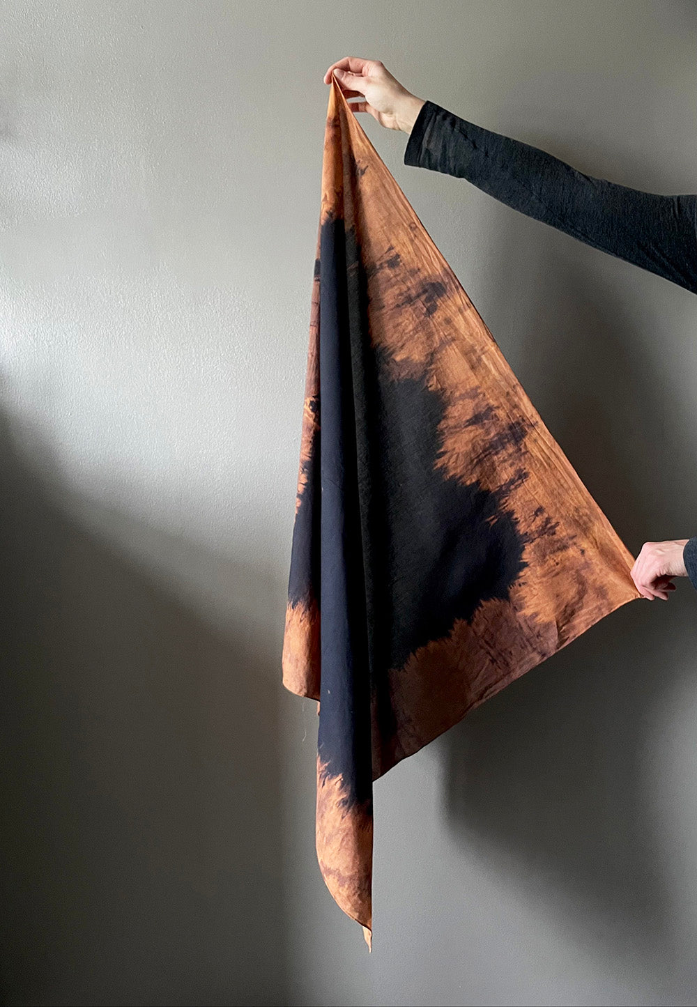 Person holding a brown and black tie-dye fabric against a gray background