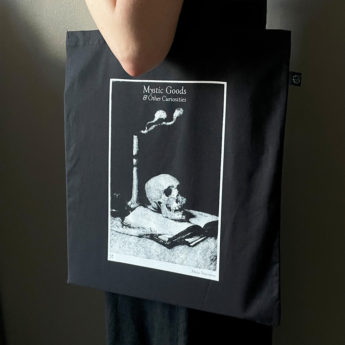 Person holding a black tote bag with a skull and candle design and text.