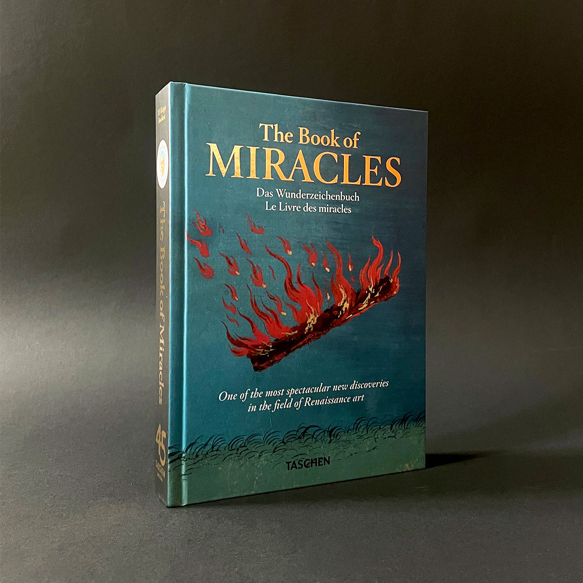 Book titled 'The Book of Miracles' with a blue cover and red flames on a dark background