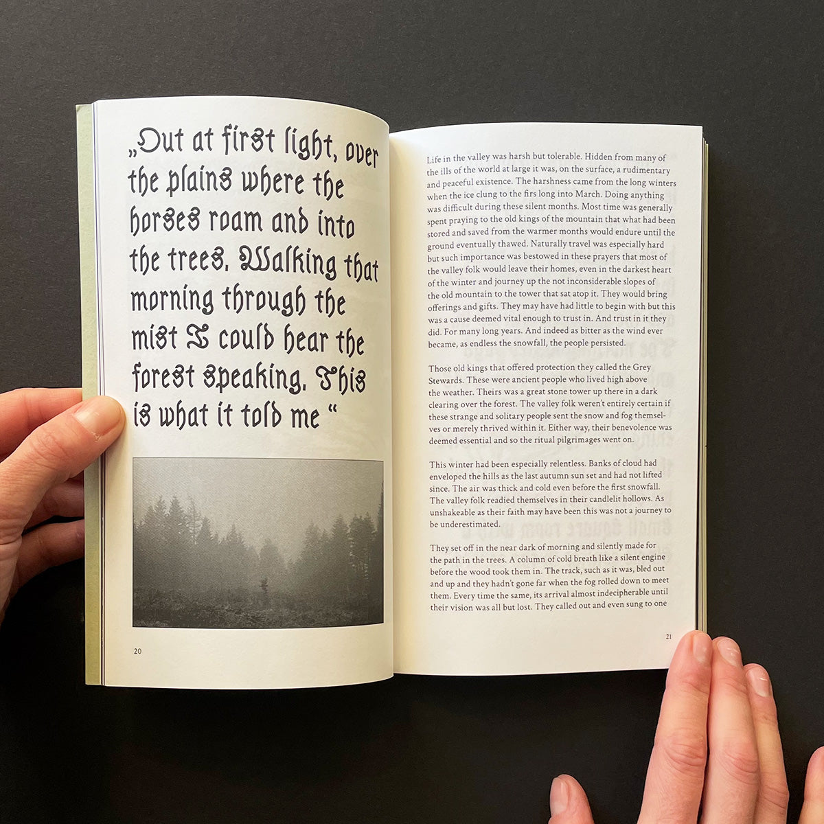 Open book with text and a black and white photo held by hands against a dark background