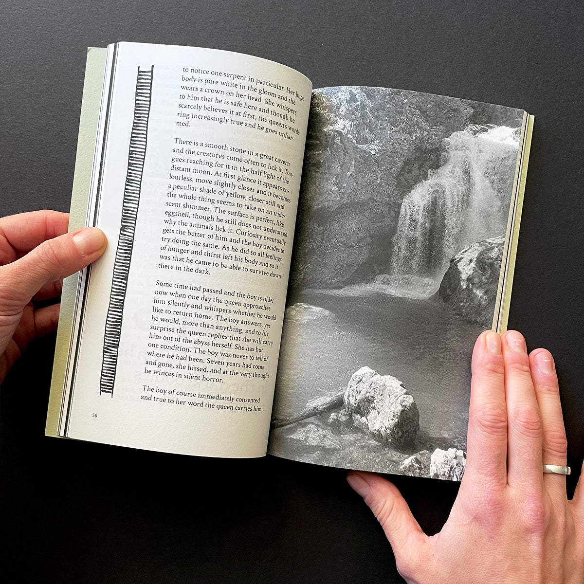 Open book held by hands with a black and white photograph of a waterfall on a dark background