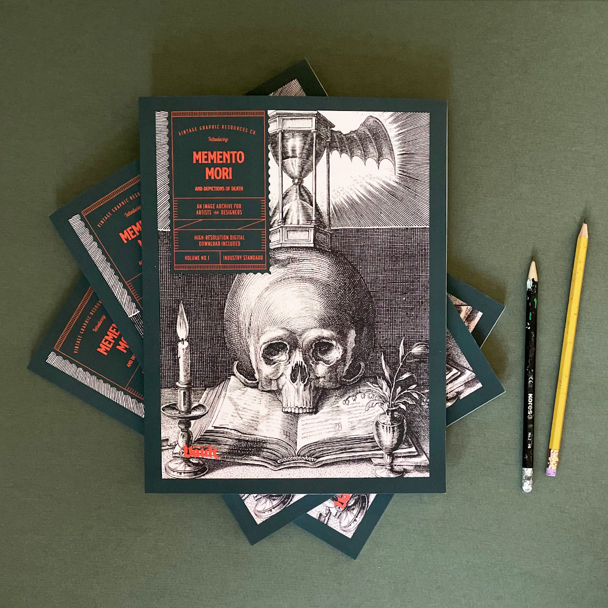 A magazine titled 'Memento Mori and Depictions of Death' featuring a black and white cover design with a skull, Hourglass, and other vintage illustrations. The book is placed on a flat surface with pencils next to it.